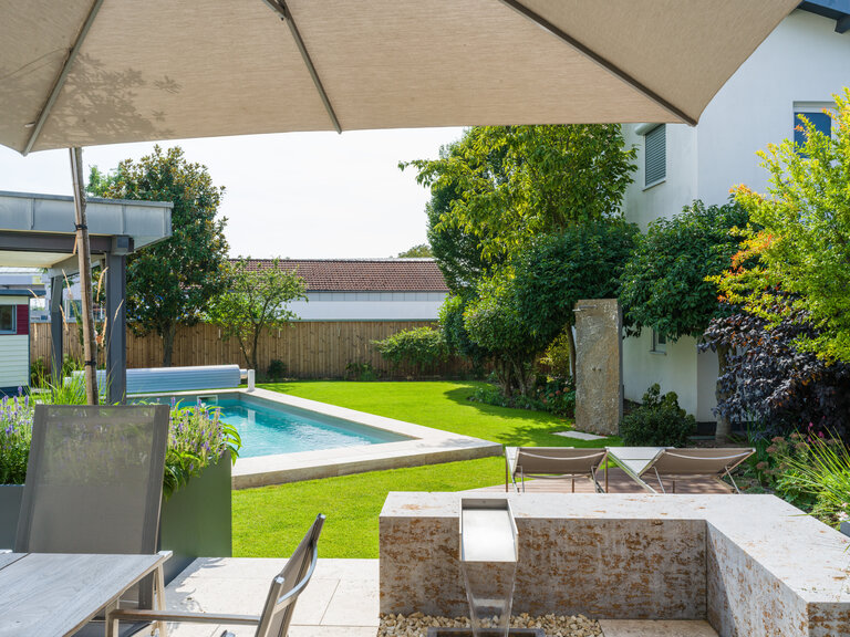 Garten mit Pool, Poolrandplatten, Wasserspiel aus Muschelkalk und Outdoor-Dusche aus Krustenplatte.