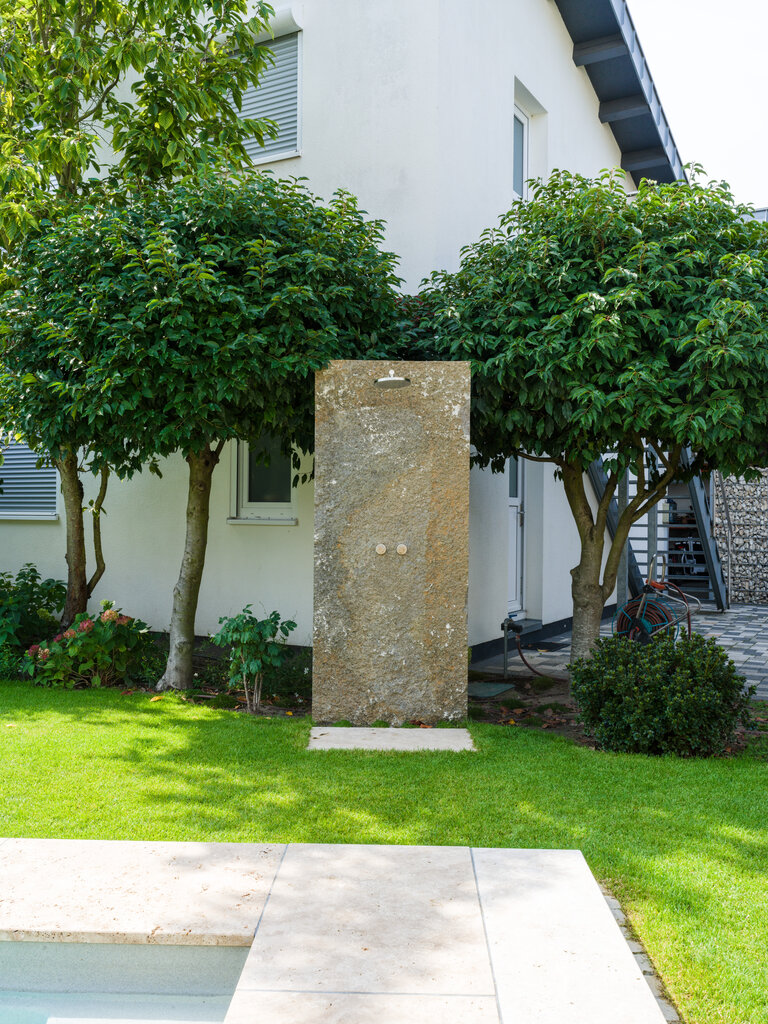 Outdoor-Dusche aus Muschelkalk Krustenplatte im Garten Outdoor-Dusche aus Muschelkalk Krustenplatte in einem Garten mit Naturstein-Elementen.