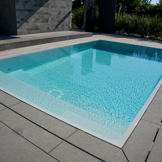 Infinity-Pool mit umlaufender Rinne und Naturstein-Randplatten mit Ablaufschlitzen.